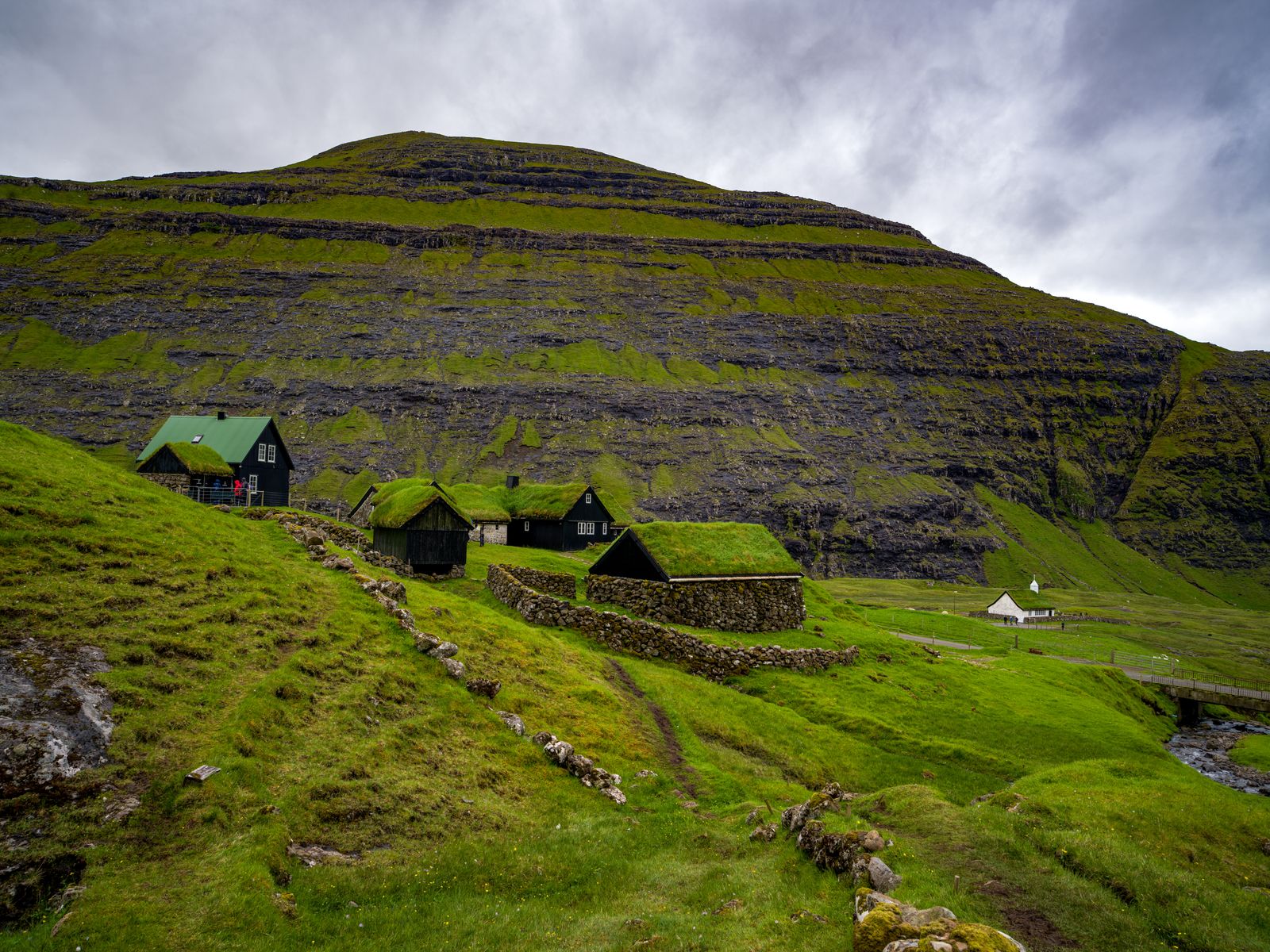Turf-roofed farm buildings and a small white church at Saksun beneath a vast cliff