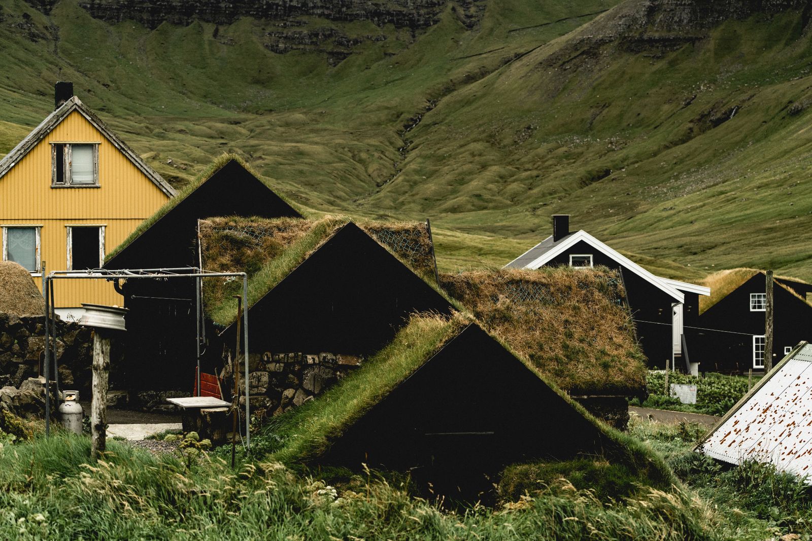 Black tarred houses with grass roofs beneath a green Faroese mountainside