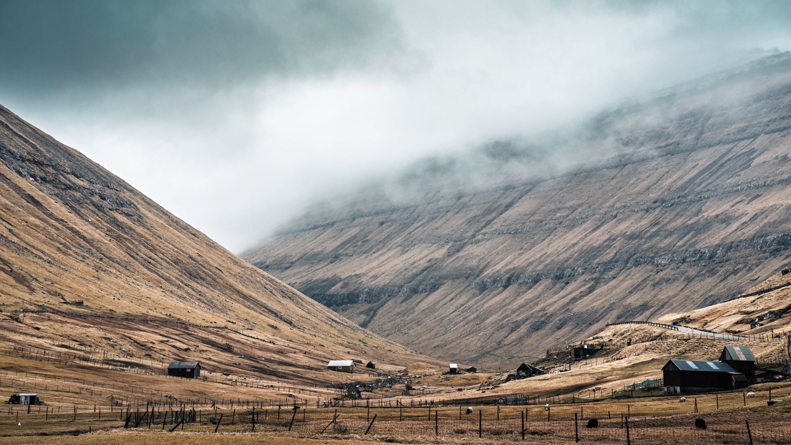 Fog rolling down a Faroese valley above a scattering of farm buildings