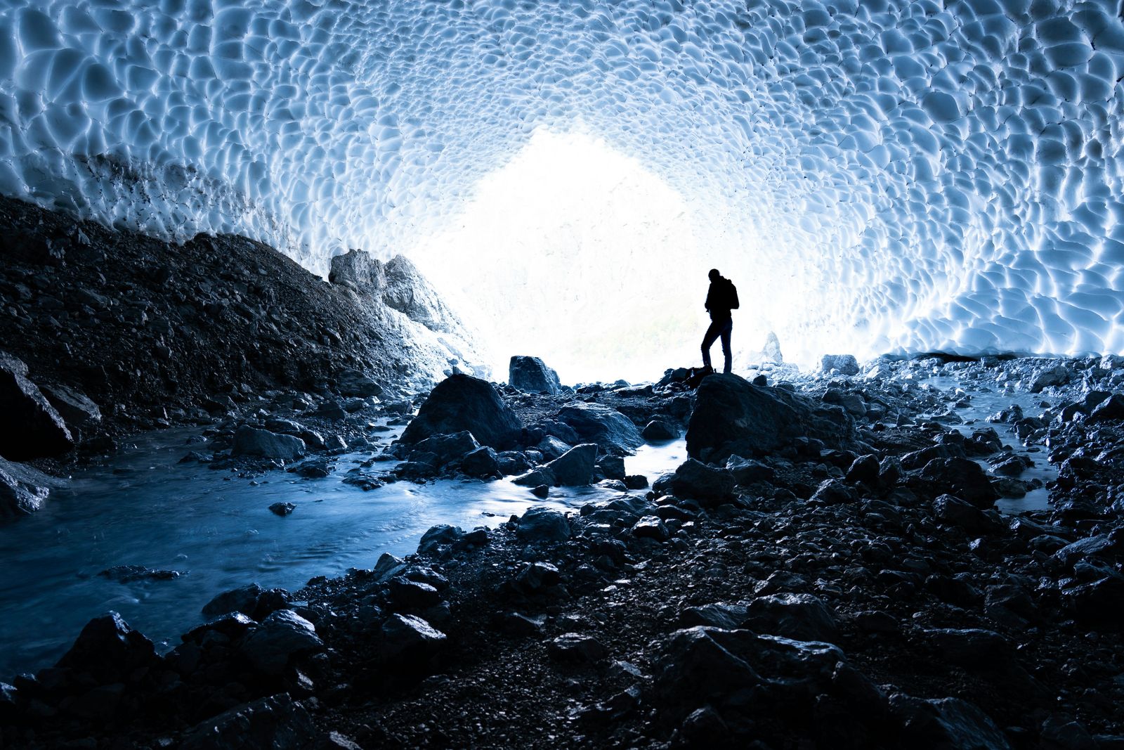 A lone figure silhouetted in a blue ice cave