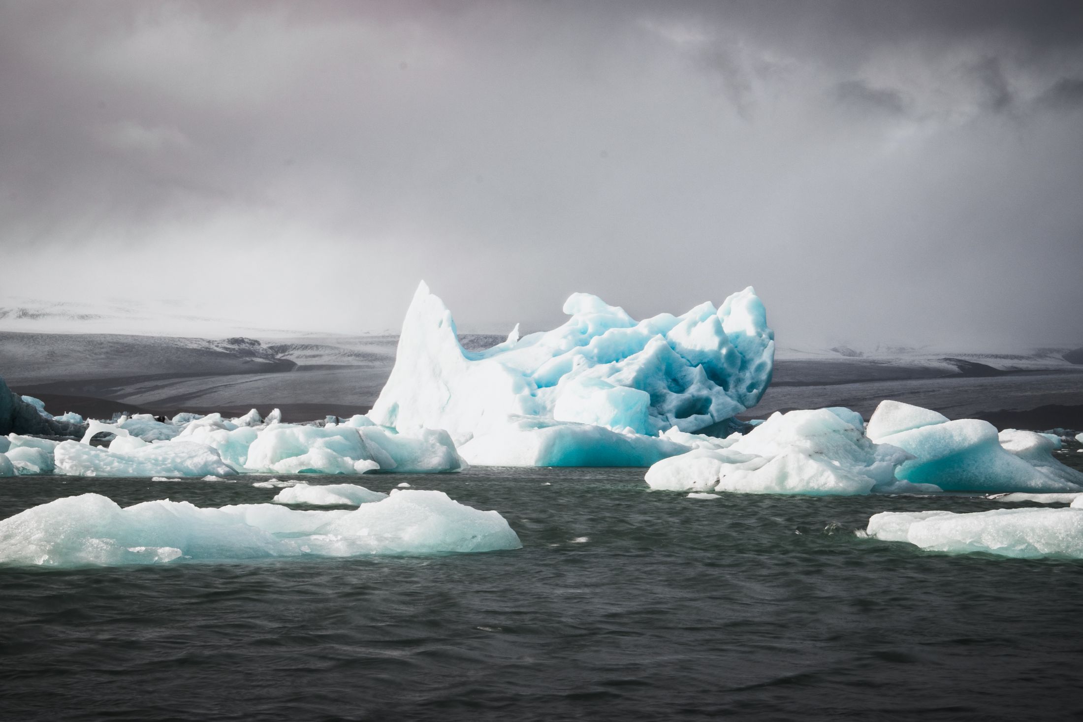 Blue icebergs glowing in an Icelandic glacier lagoon beneath a storm sky