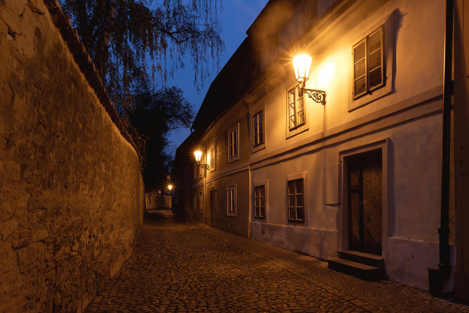 A lamplit cobblestone lane winding between old houses